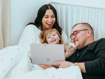 parents and child happily looking at tablet in a bed
